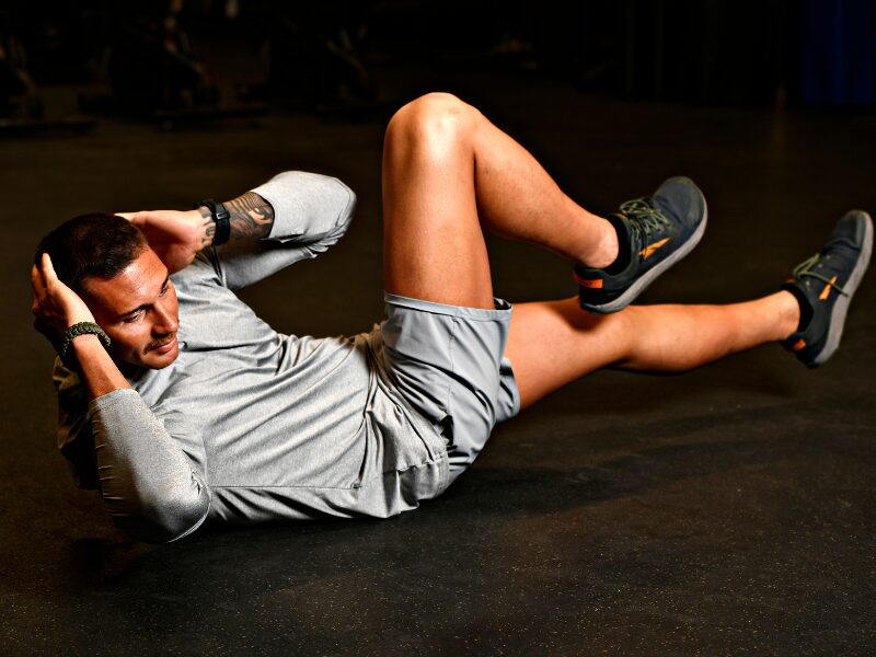 Man dressed in gray shorts and gray shirt demonstrates how to do a proper bicycle crunch exercise.